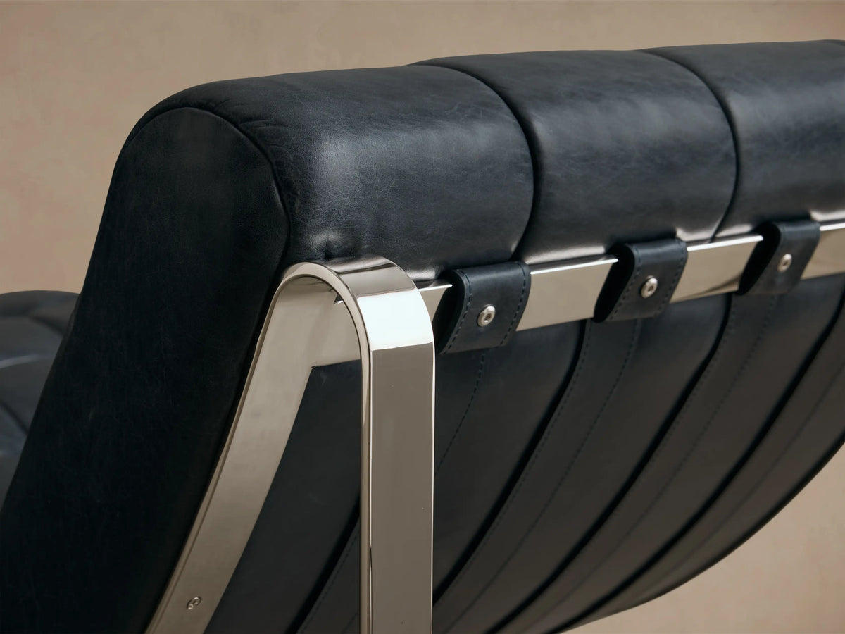 Close-up of the black leather Callaway Leather Chaise, featuring padded horizontal cushions and a curved, polished silver metal frame.