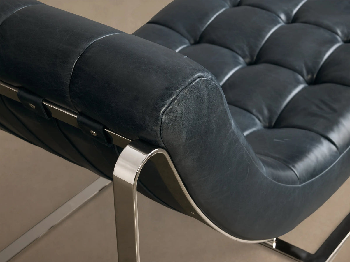 Front view of the dark blue tufted Callaway Leather Chaise, featuring a curved design and polished chrome frame.