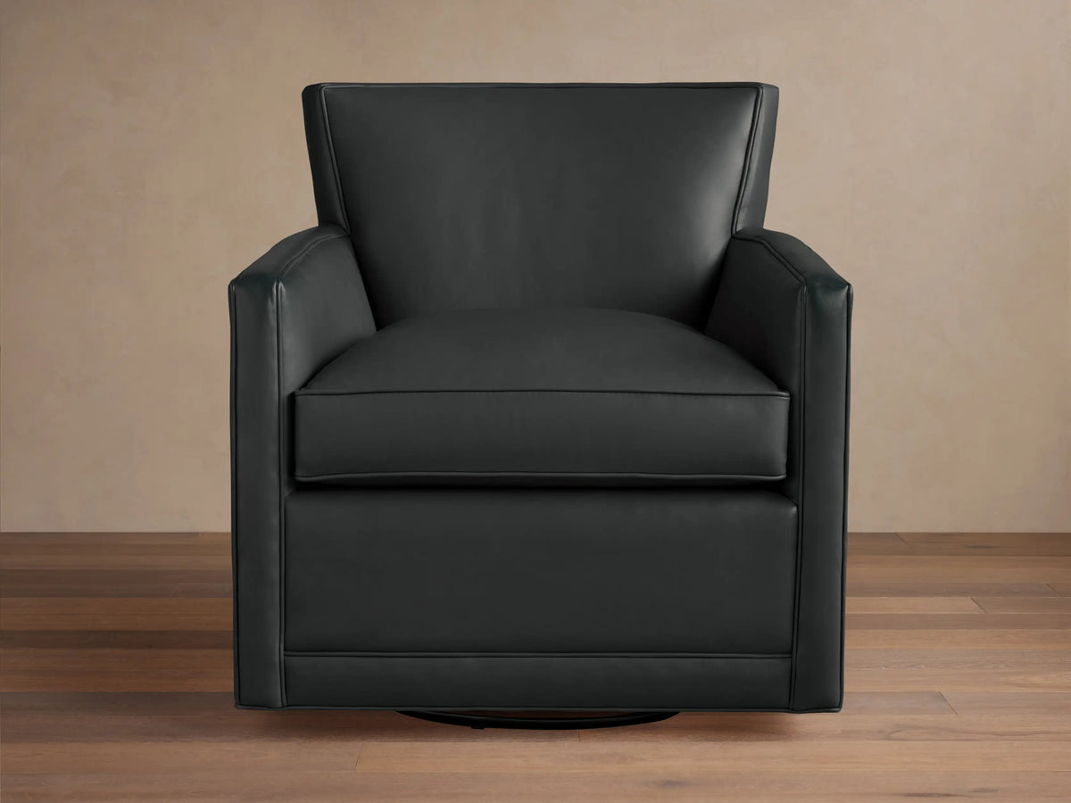 Black leather Rudy Swivel Chair with a modern, clean design, square arms, shown on a wooden floor against a light wall.