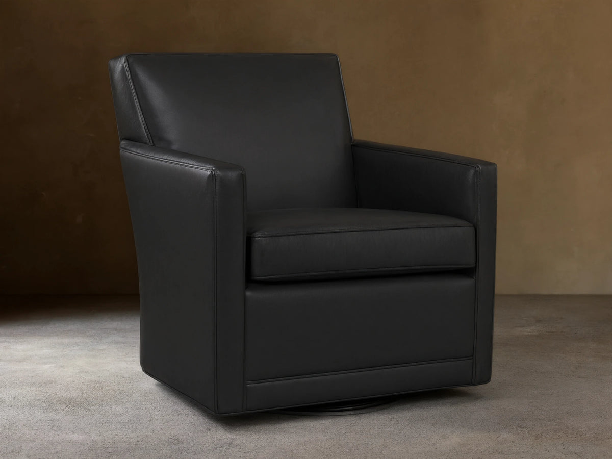 Black leather Rudy Swivel Chair with a modern, clean design, square arms, shown on a wooden floor against a light wall.