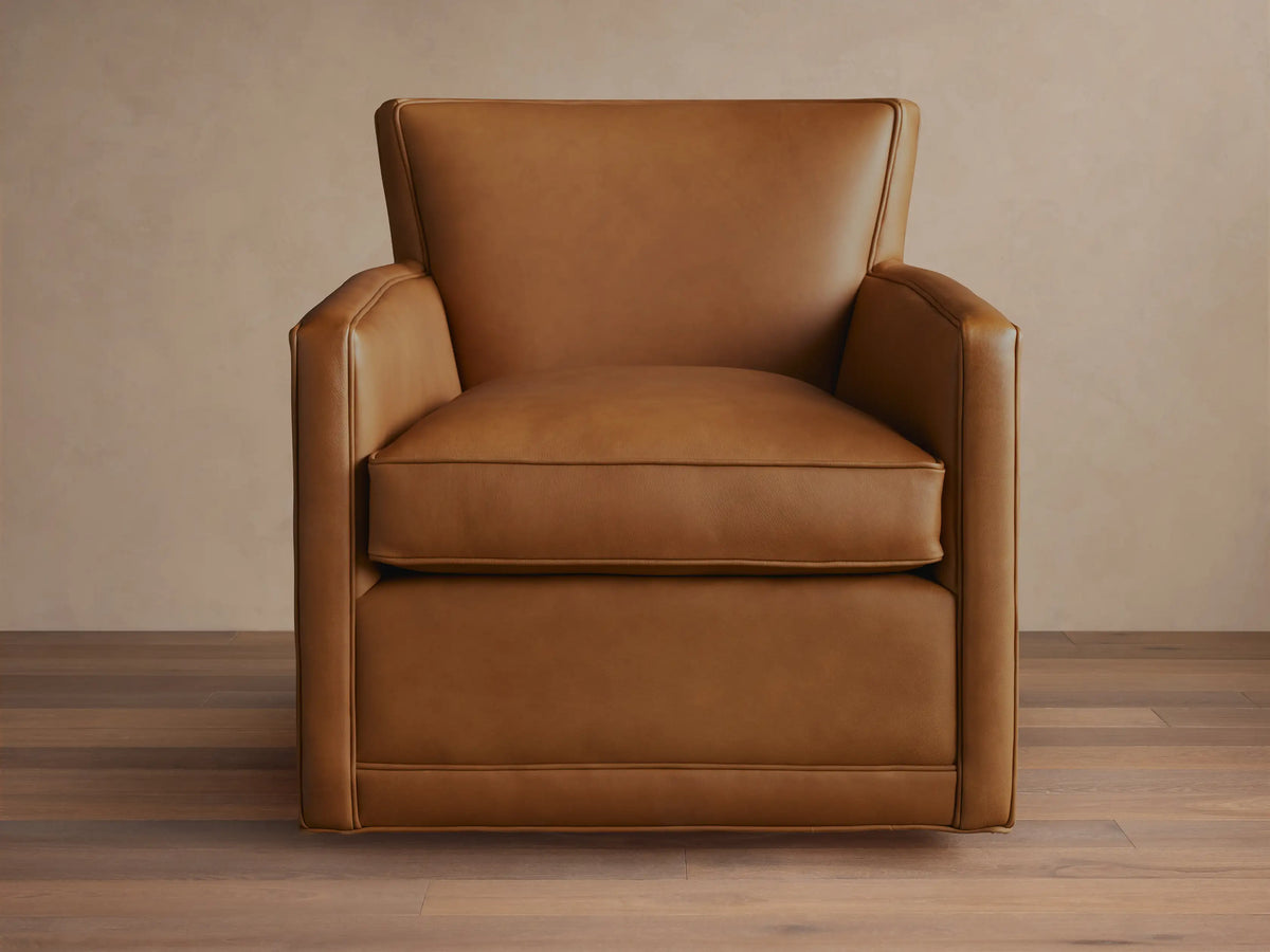 Caramel brown Rudy Leather Swivel Chair, front view, with square arms, loose seat cushion, piping details, on a black swivel base.