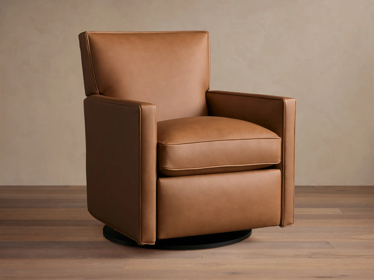 Tan leather Rudy swivel recliner, square arms & back, with a plump seat cushion, on a dark round swivel base, on wood floor.