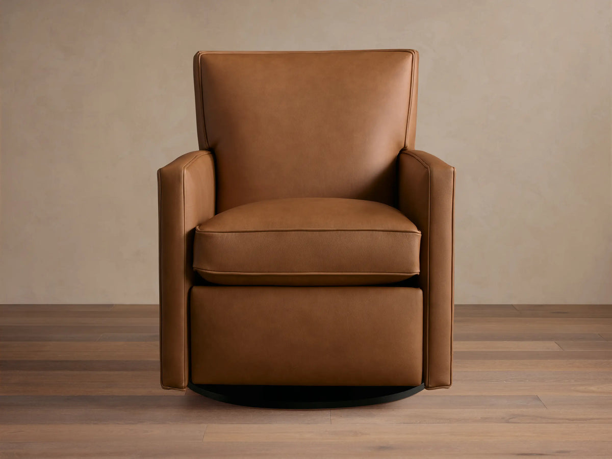 Tan leather Rudy swivel recliner, square arms & back, with a plump seat cushion, on a dark round swivel base, on wood floor.