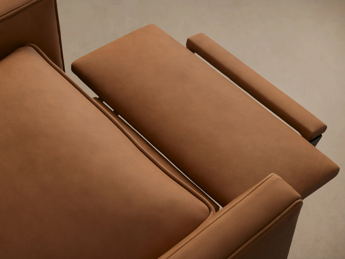 Front view of a warm brown leather Rudy Swivel Recliner with padded arms & cushions, on a black swivel base on wood floor.