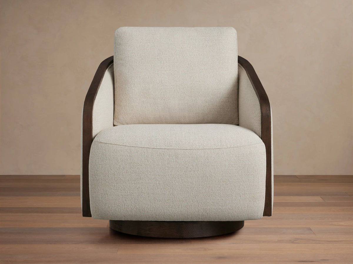Front-side view of a neutral beige Pomona Swivel Chair with dark wood exposed edges on its arms and base.