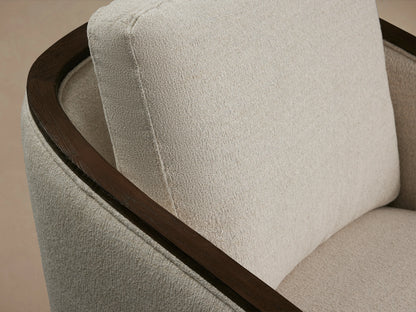 Pomona Swivel Chair with light beige fabric, dark wood exposed arms, and base, on wooden floor against a neutral wall.
