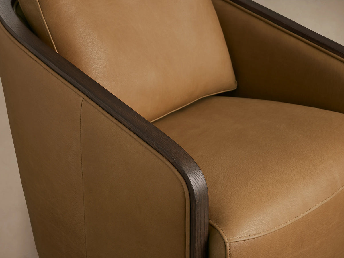 Pomona Leather Swivel Chair in tan leather with dark oak arms and base. Front view showing plush seat and backrest. On wooden floor.
