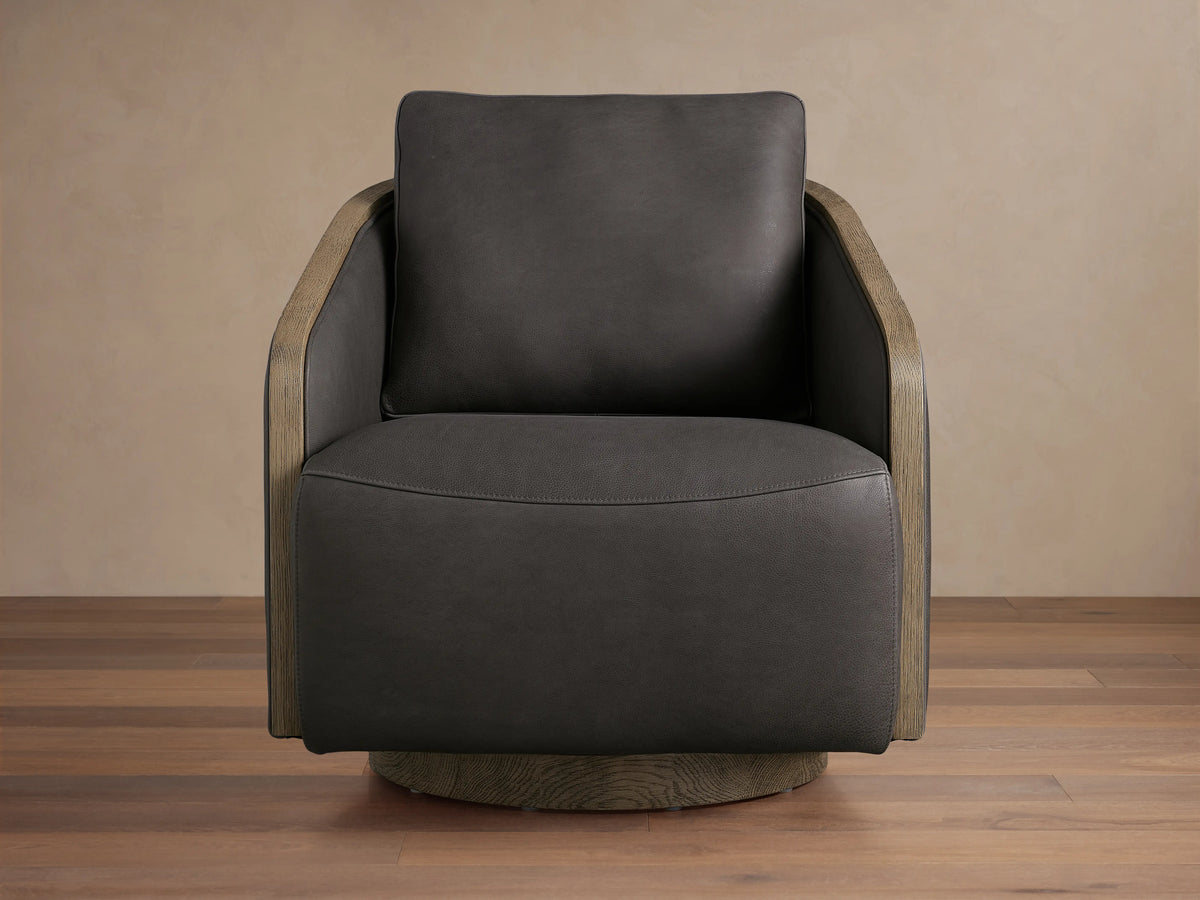Dark brown leather swivel chair with exposed oak edges on arms and base, featuring soft cushioned seat and backrest on wooden floor.