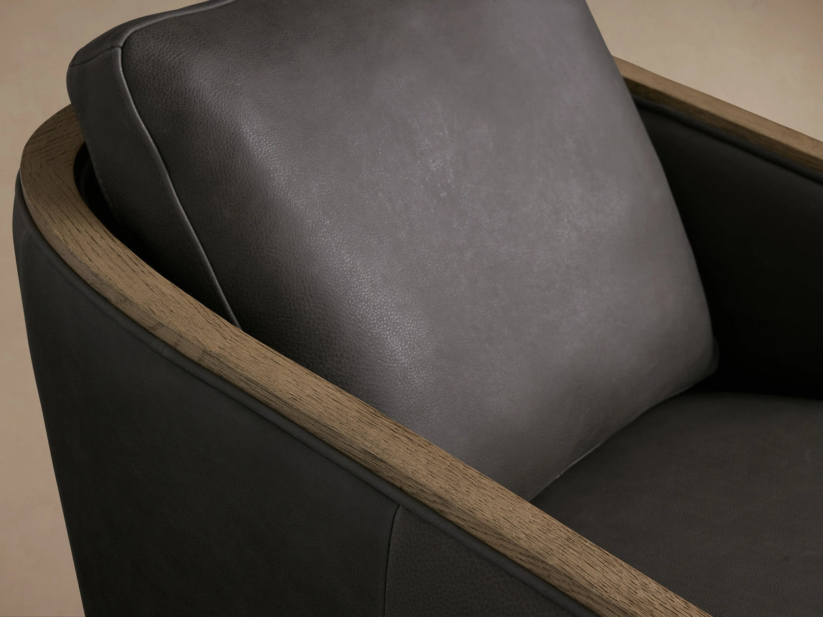 Pomona Leather Swivel Chair with dark leather cushions and exposed oak edges, front view on wood floor, against a neutral background.