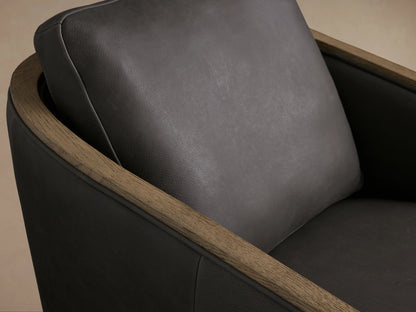 Pomona Leather Swivel Chair with dark leather cushions and exposed oak edges, front view on wood floor, against a neutral background.
