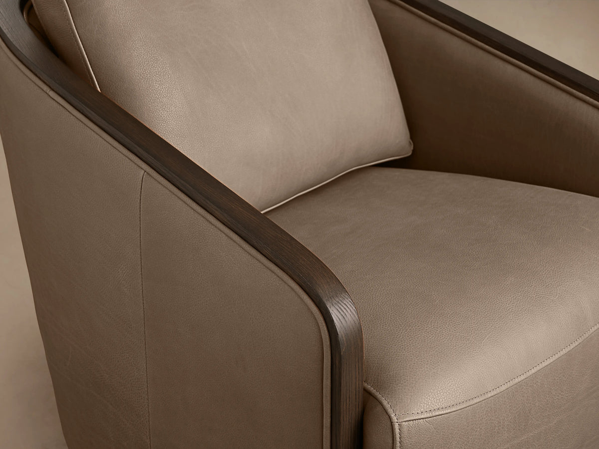 Pomona Leather Swivel Chair in beige leather with exposed oak edges, featuring rounded back, armrests, and a swivel base on a wooden floor.