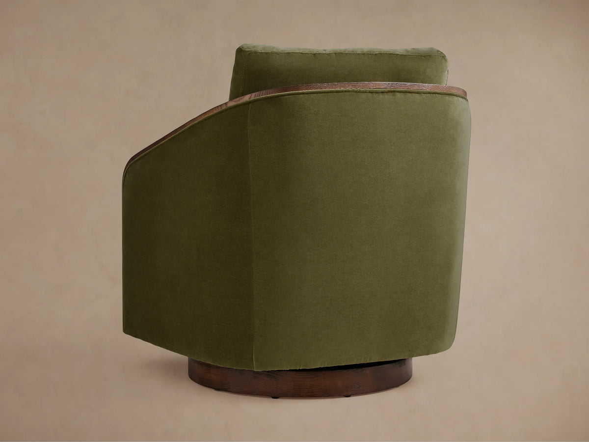 The Pomona Swivel Chair in olive green, side view, with exposed oak edges and a dark wood swivel base on a beige background.