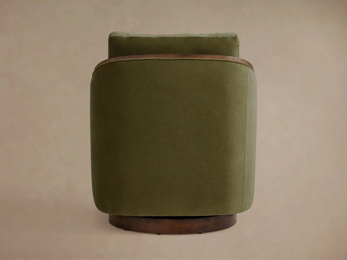 The Pomona Swivel Chair in olive green fabric, featuring oak edges on arms and base, viewed from an angle showing its solid form.