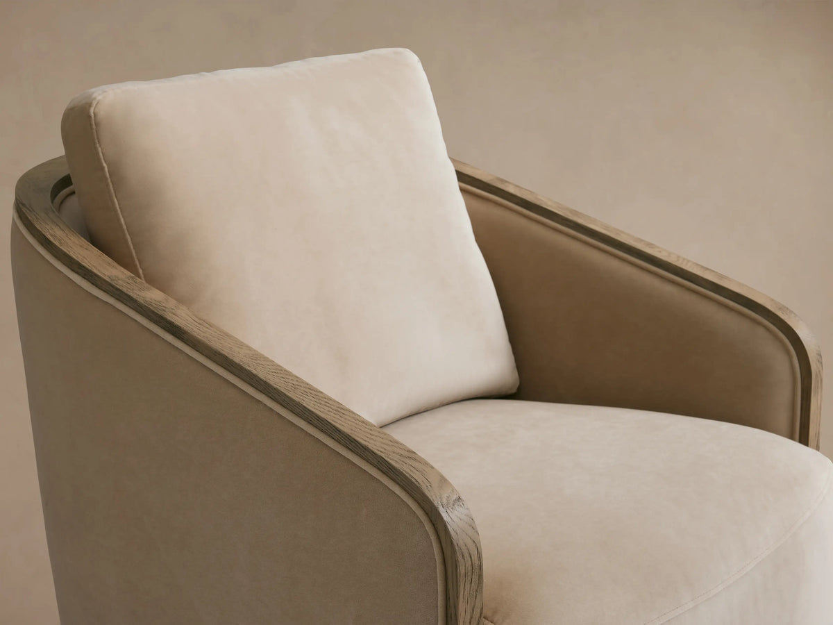 Pomona Swivel Chair in neutral beige with soft cushions and exposed oak edges on arms and base, on wooden floor.