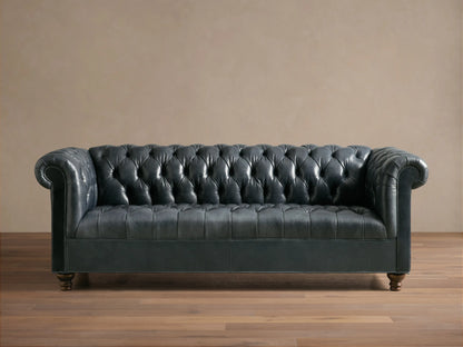 Front view of the dark blue-gray Berwick Leather Sofa, featuring a button-tufted back, rolled arms, and carved walnut legs.