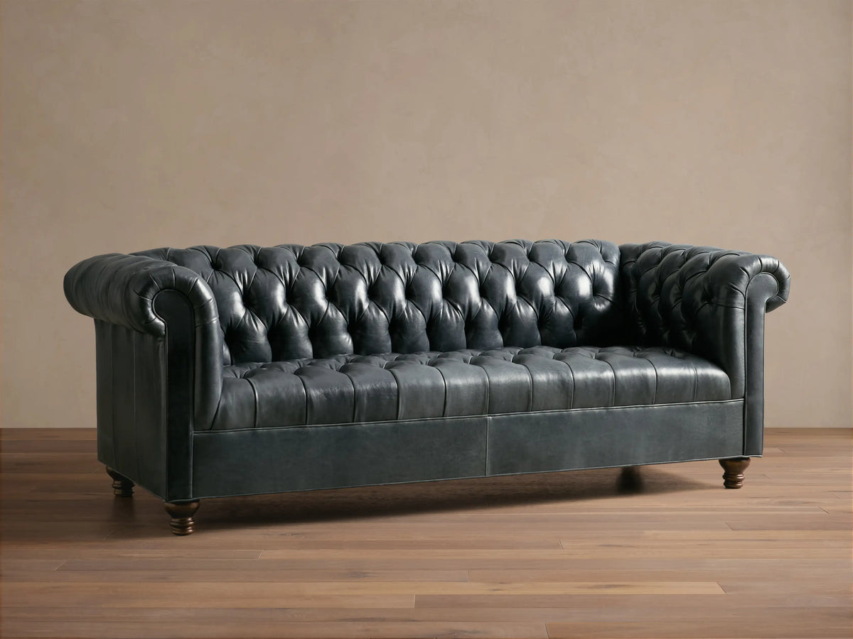Front view of the dark blue-gray Berwick Leather Sofa, featuring a button-tufted back, rolled arms, and carved walnut legs.