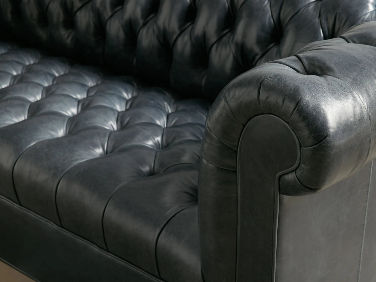 Front view of the dark gray tufted Berwick Leather Sofa with rolled arms and turned wooden legs.