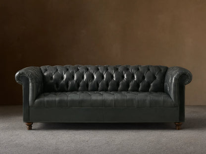 Front view of the dark blue-gray Berwick Leather Sofa, featuring a button-tufted back, rolled arms, and carved walnut legs.