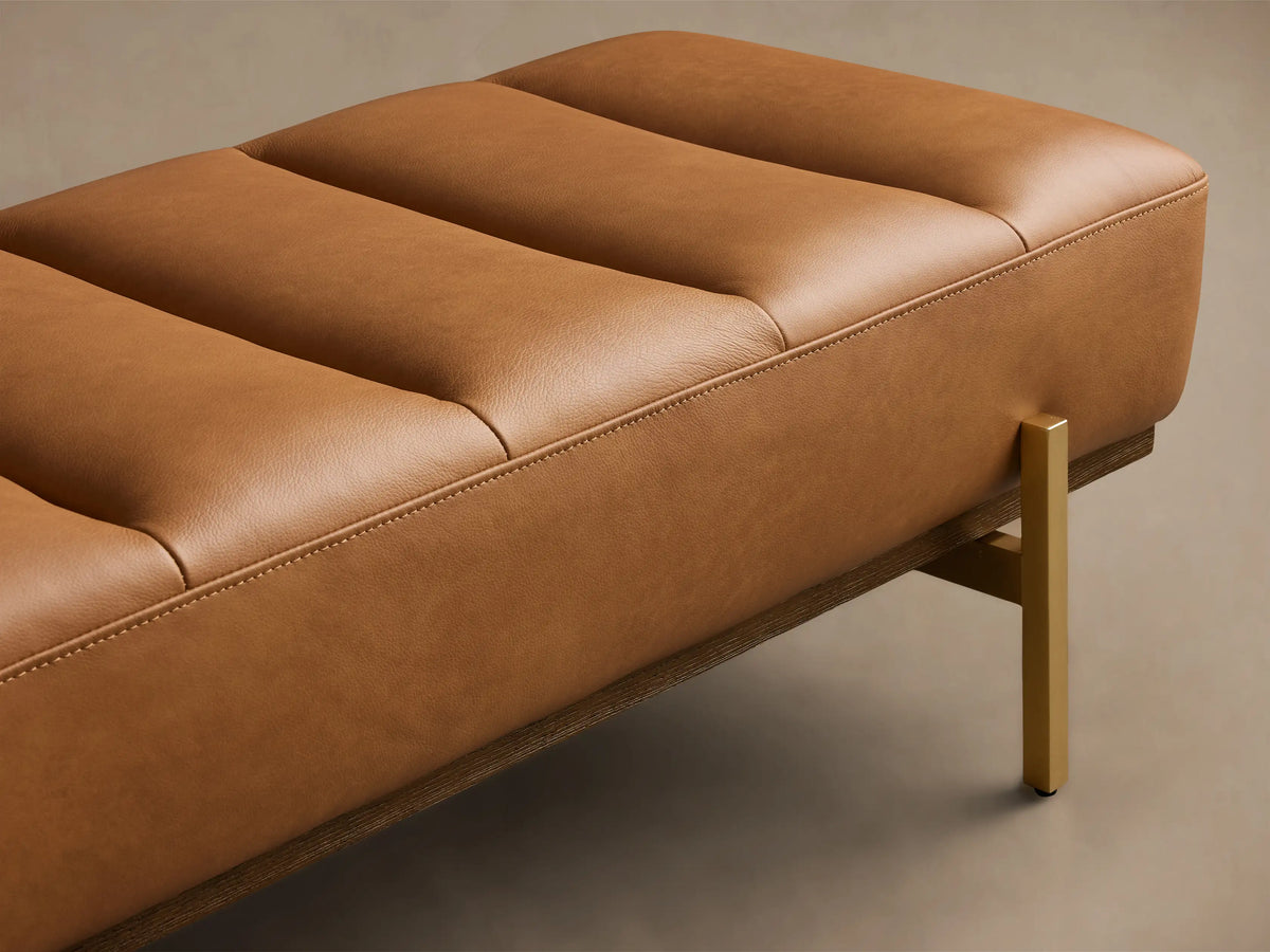 Front view of a camel leather channel tufted bench with a dark wood base and gold-finished legs.
