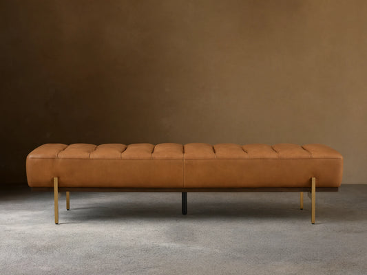 Front view of a camel leather tufted bench with a dark wood base and slender gold-toned metal legs.