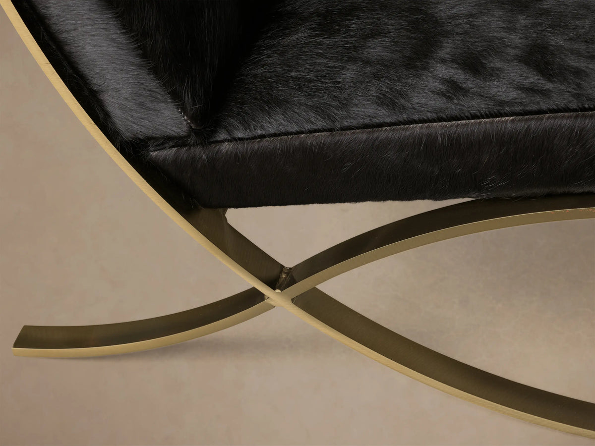 Front view of the Black Moxie Hair on Hide Chair with a square, tufted seat and back, and brass-finish x-shaped legs.