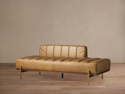 Lansing Leather Daybed with tan channel-tufted leather, low backrest on left, dark wood base, and gold legs on wood floor.