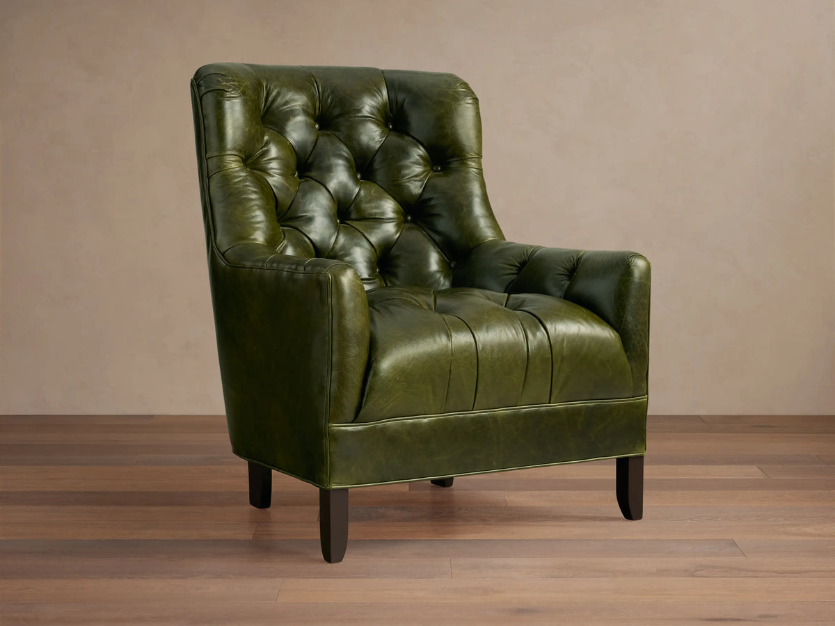 Olive green leather Club Chair with a deep tufted backrest, wide arms, and dark wooden legs, angled on a wood floor.