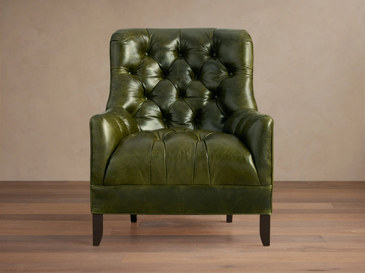 Olive green leather Club Chair with a deep tufted backrest, wide arms, and dark wooden legs, angled on a wood floor.