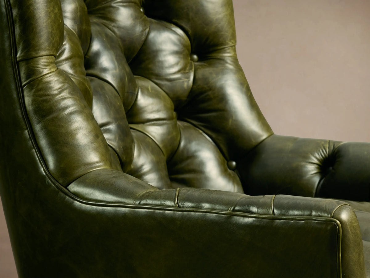 Front view of a vintage-style green leather club chair with deep tufting, padded arms, and dark wooden legs.