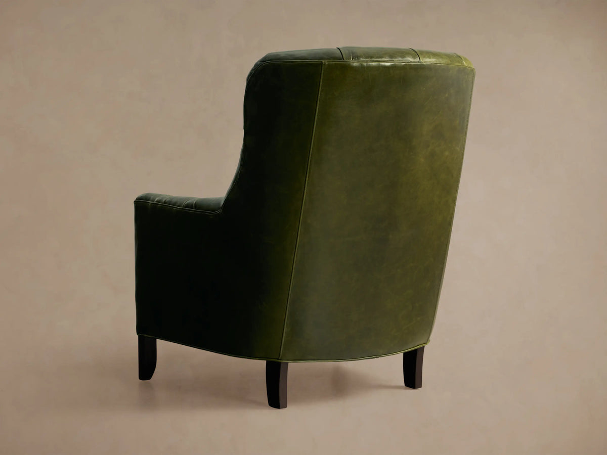 Angled close-up of a distressed olive green Club Leather Chair, featuring its tufted back, buttons, and rounded armrest.