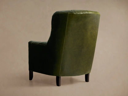 Angled close-up of a distressed olive green Club Leather Chair, featuring its tufted back, buttons, and rounded armrest.