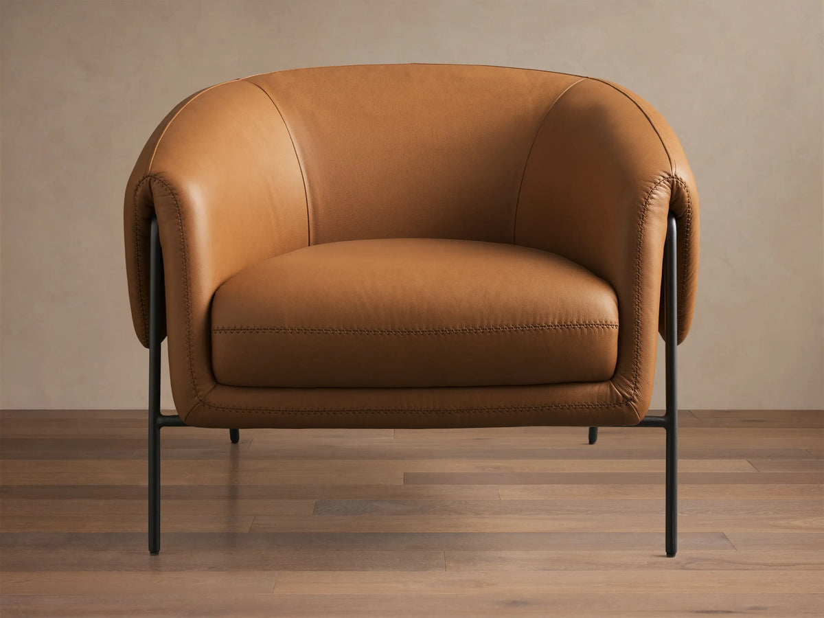 Front view of the Caramel Linus Leather Chair, featuring a curved back, stitched cushions, and sleek black metal legs.