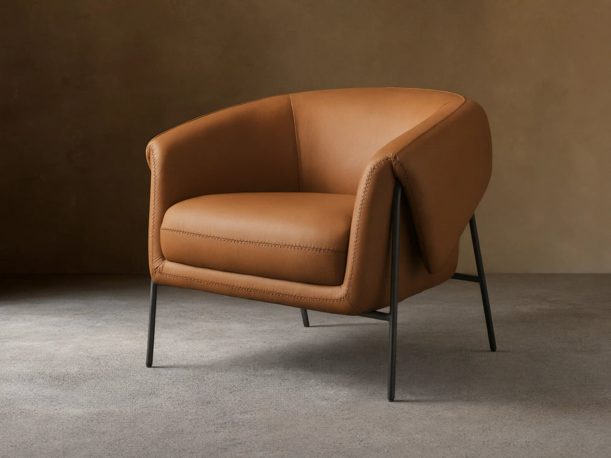 Front view of a Caramel Linus Leather Chair with a curved back, prominent stitching, and sleek black metal legs.