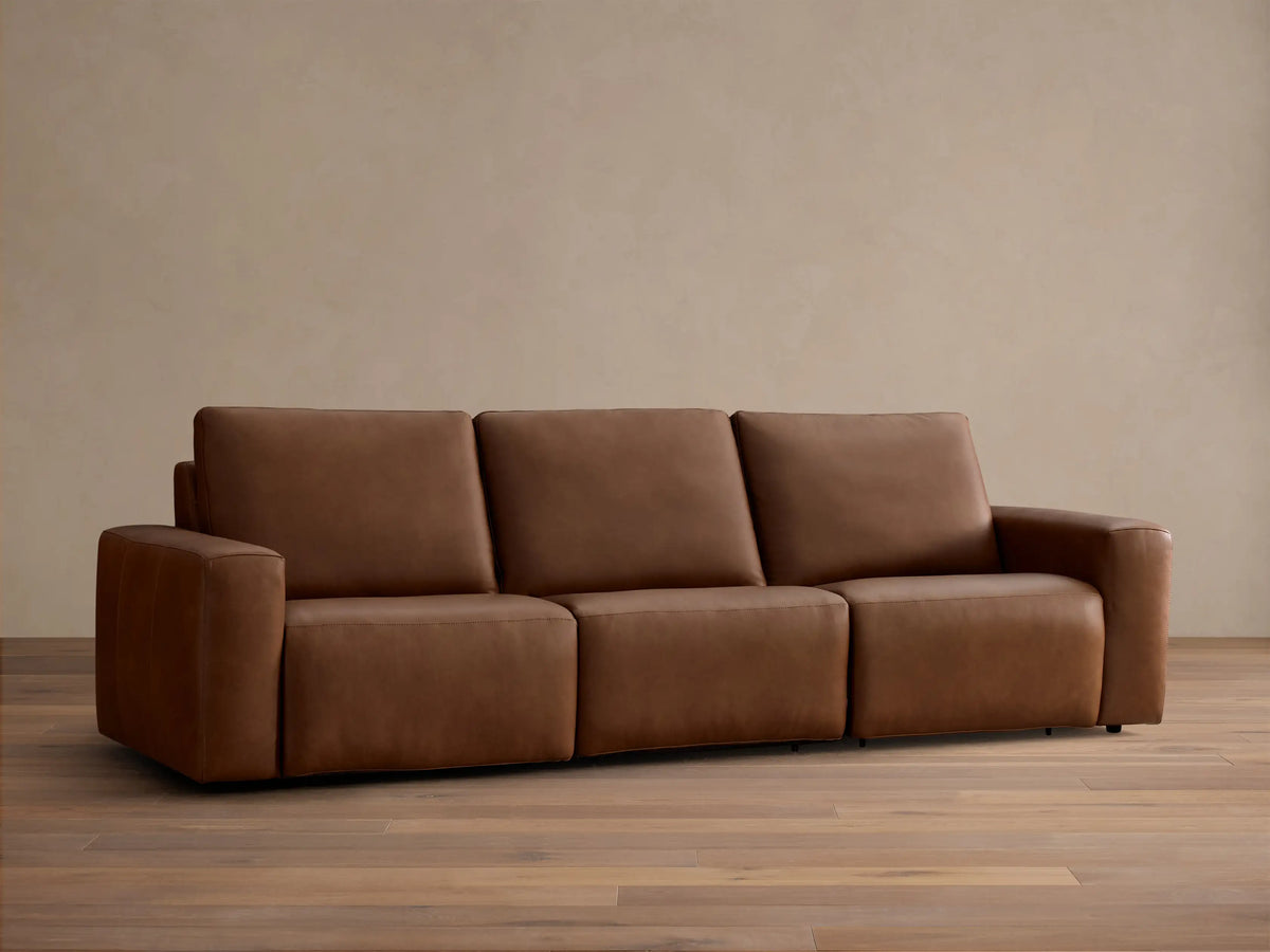 Front view of the brown Brennan Leather Three-Piece Motion Sofa, displaying its integrated design with wide arms and plush seats.