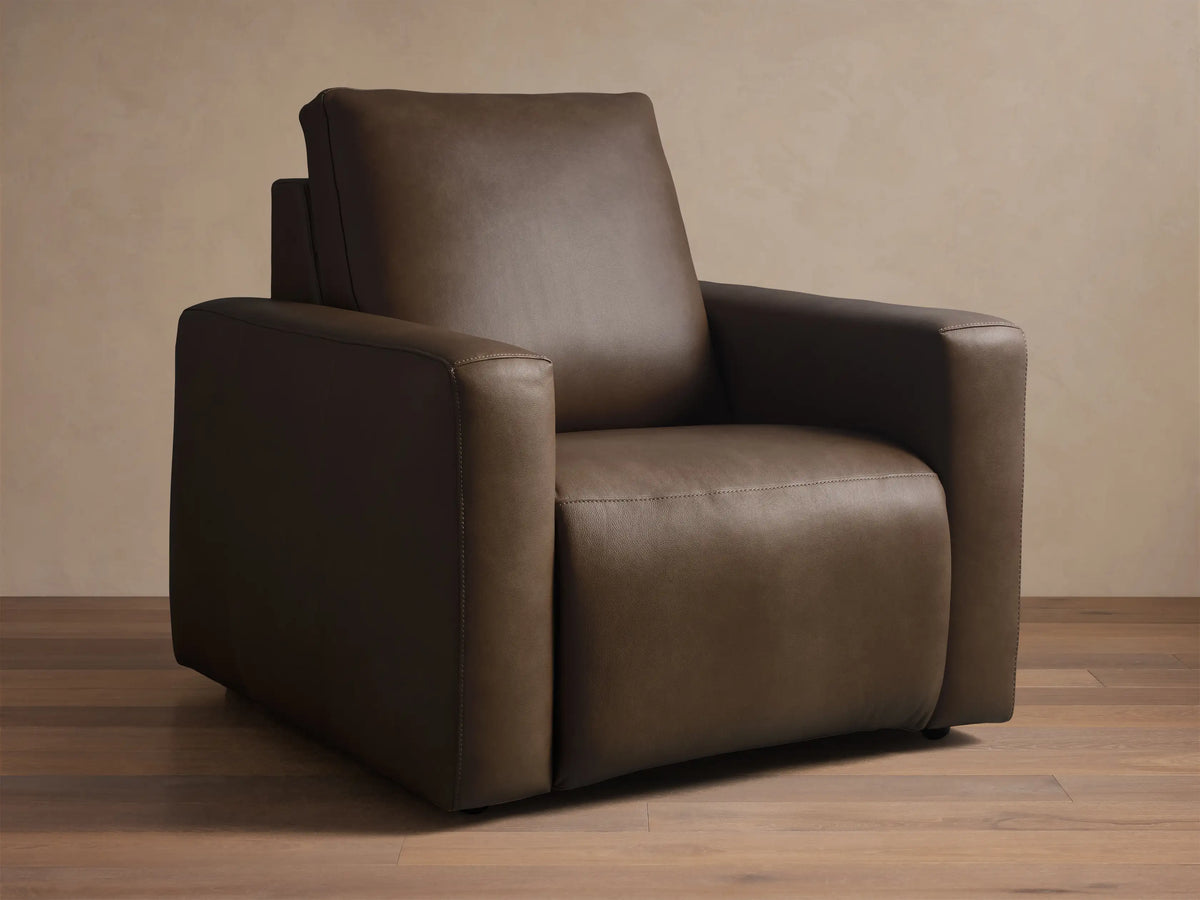 Close-up, angled view of the brown Brennan Leather Motion Recliner, highlighting the leather texture and detailed stitching on the armrest and seat.