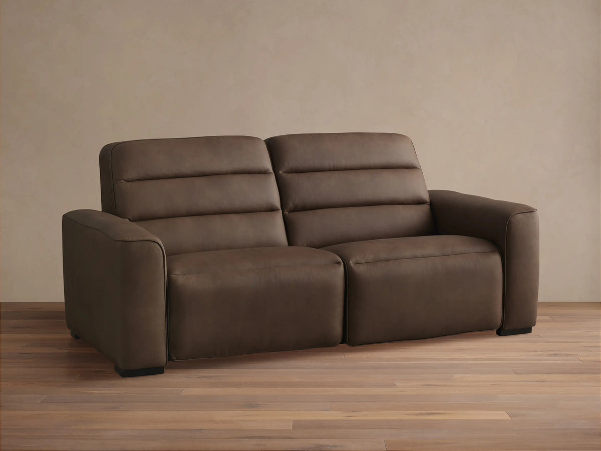 Borough Two-Piece Motion Sofa in dark brown leather, front view. Two distinct seats with horizontal padded backrests, on a light wood floor.