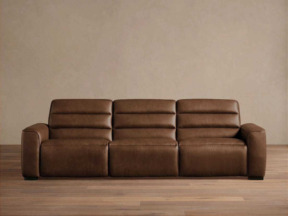 Front view of Borough Three-Piece Motion Sofa in rich brown leather, featuring plush, segmented cushions, on a wood floor.