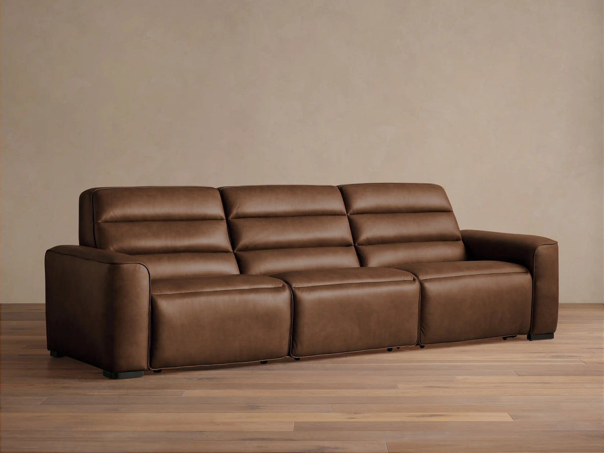 Front view of Borough Three-Piece Motion Sofa in rich brown leather, featuring plush, segmented cushions, on a wood floor.