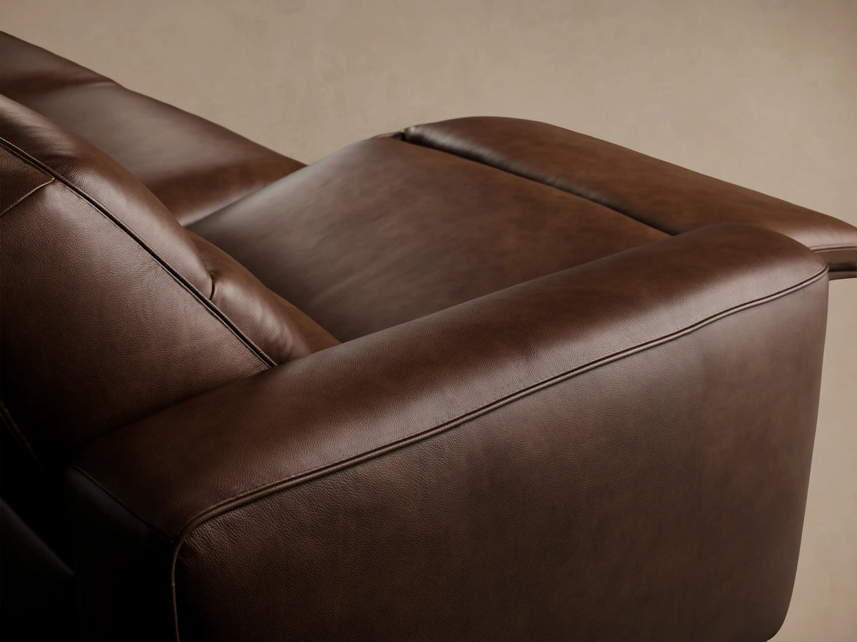 Borough Leather Four-Piece Motion Sectional, a long brown leather sofa with four reclining seats, against a beige wall on a wood floor.