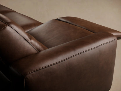 Borough Leather Four-Piece Motion Sectional, a long brown leather sofa with four reclining seats, against a beige wall on a wood floor.