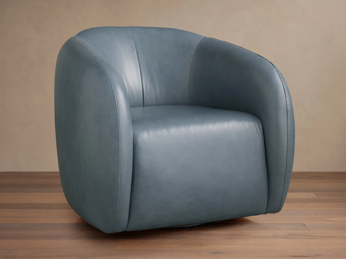 Fresno Leather Swivel Chair in blue-gray leather, featuring a curved, padded backrest and seat on a wooden floor, facing slightly left.
