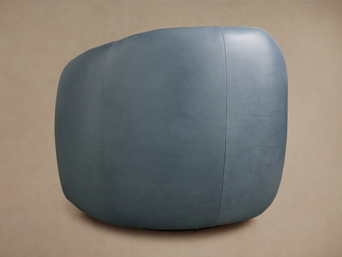 A side view of the Fresno Leather Swivel Chair in light blue leather, highlighting its smooth, curved backrest against a beige background.
