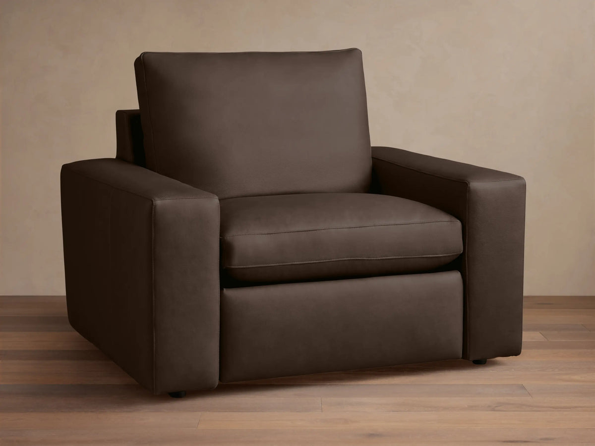 Wide arm leather motion recliner in dark brown leather, with plush seat and back cushions, on a wooden floor background.