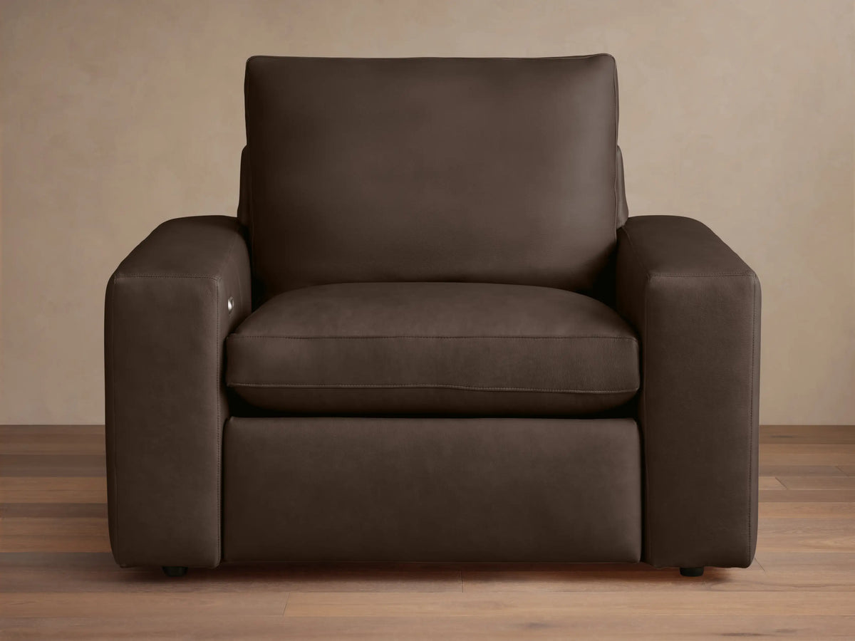 Wide arm leather motion recliner in dark brown leather, with plush seat and back cushions, on a wooden floor background.