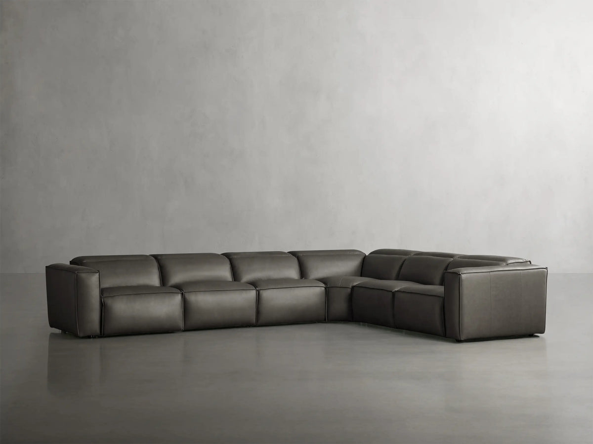 Coburn six-piece L-shaped sectional in dark grey leather, featuring plush seats and sleek design against a minimalist grey backdrop.