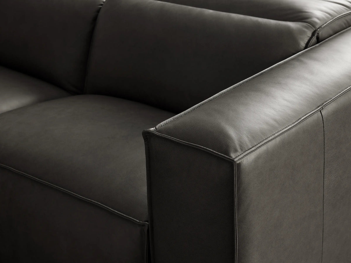 Dark gray leather L-shaped Coburn Six Piece Motion Sectional, viewed from front-right, on a gray floor in a minimalist setting.