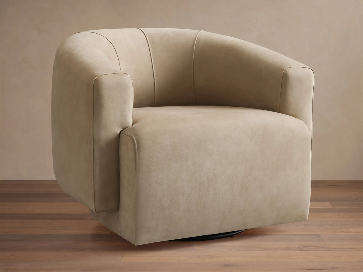 Hamlin Nubuck Leather Swivel Chair in beige, featuring a curved backrest and armrests, set on a wooden floor with a neutral backdrop.