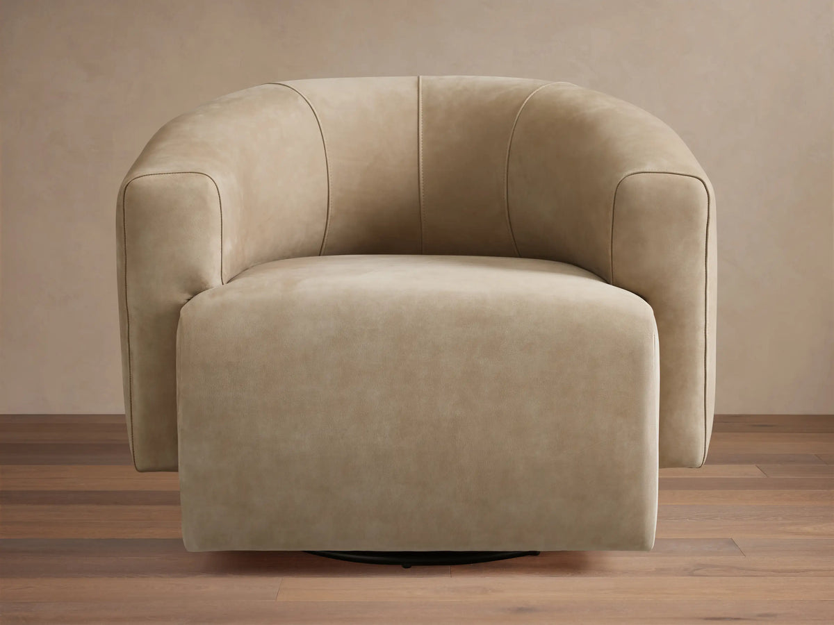 Hamlin Nubuck Leather Swivel Chair in beige, featuring a curved backrest and armrests, set on a wooden floor with a neutral backdrop.