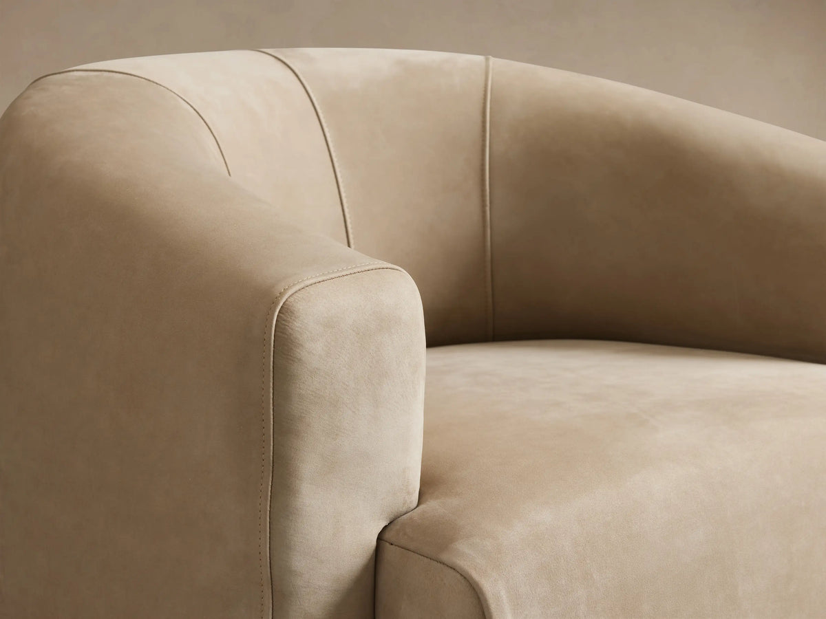 Beige Hamlin Nubuck Leather Swivel Chair with rounded backrest and seat cushion on a wooden floor, facing forward with a seamless design.