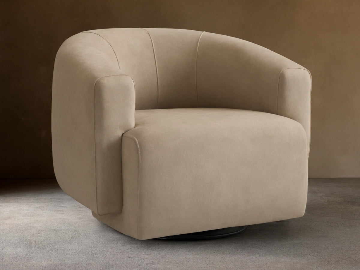 Hamlin Nubuck Leather Swivel Chair in beige, featuring a curved backrest and armrests, set on a wooden floor with a neutral backdrop.